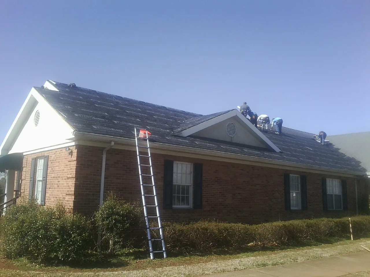 Crew tearing shingles off a brick ranch roof with a ladder set — Emergency Roof Repair work by our crew in Westfir