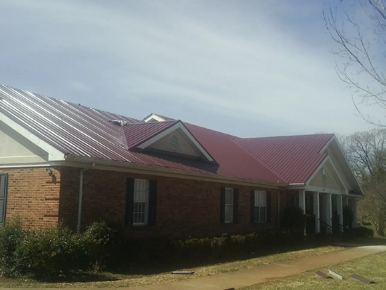 Red metal roof with gabled entries on a long brick building, from a Hail Damage Roof Repair job in Westfir