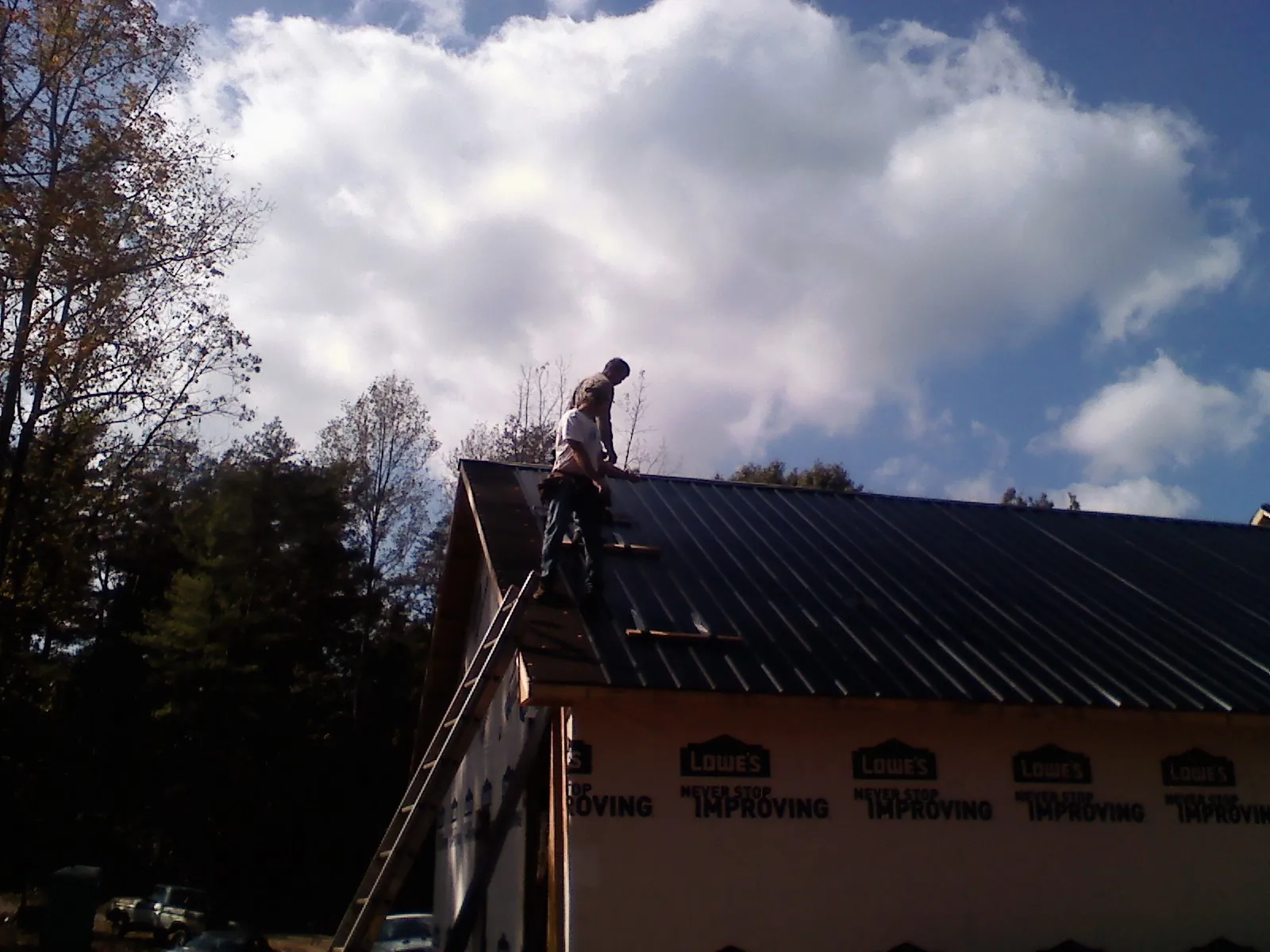Roofer fastening dark metal panels high against a cloudy sky, from a Roof Inspection job in Westfir