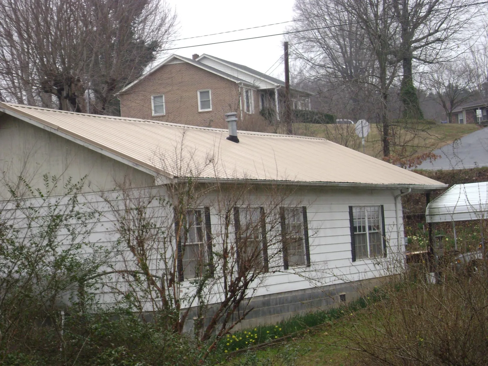 Tan metal roof on a white sided house set into a hillside — Commercial Roofing by Roofing Brothers in Westfir